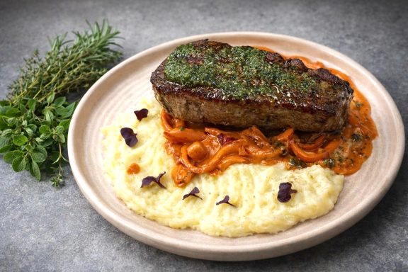 Ein saftiges Steak auf einem Bett aus pürierten Kartoffeln und einer Tomatensauce.