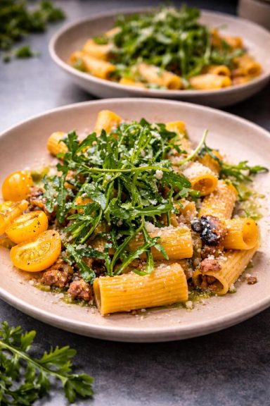 Pasta mit Wurst, Kirschtomaten und frischem Rucola auf einem Teller.