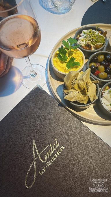 Ein Tisch mit Tapas, Oliven, Dips und einem Glas Roséwein, daneben eine Menükarte.